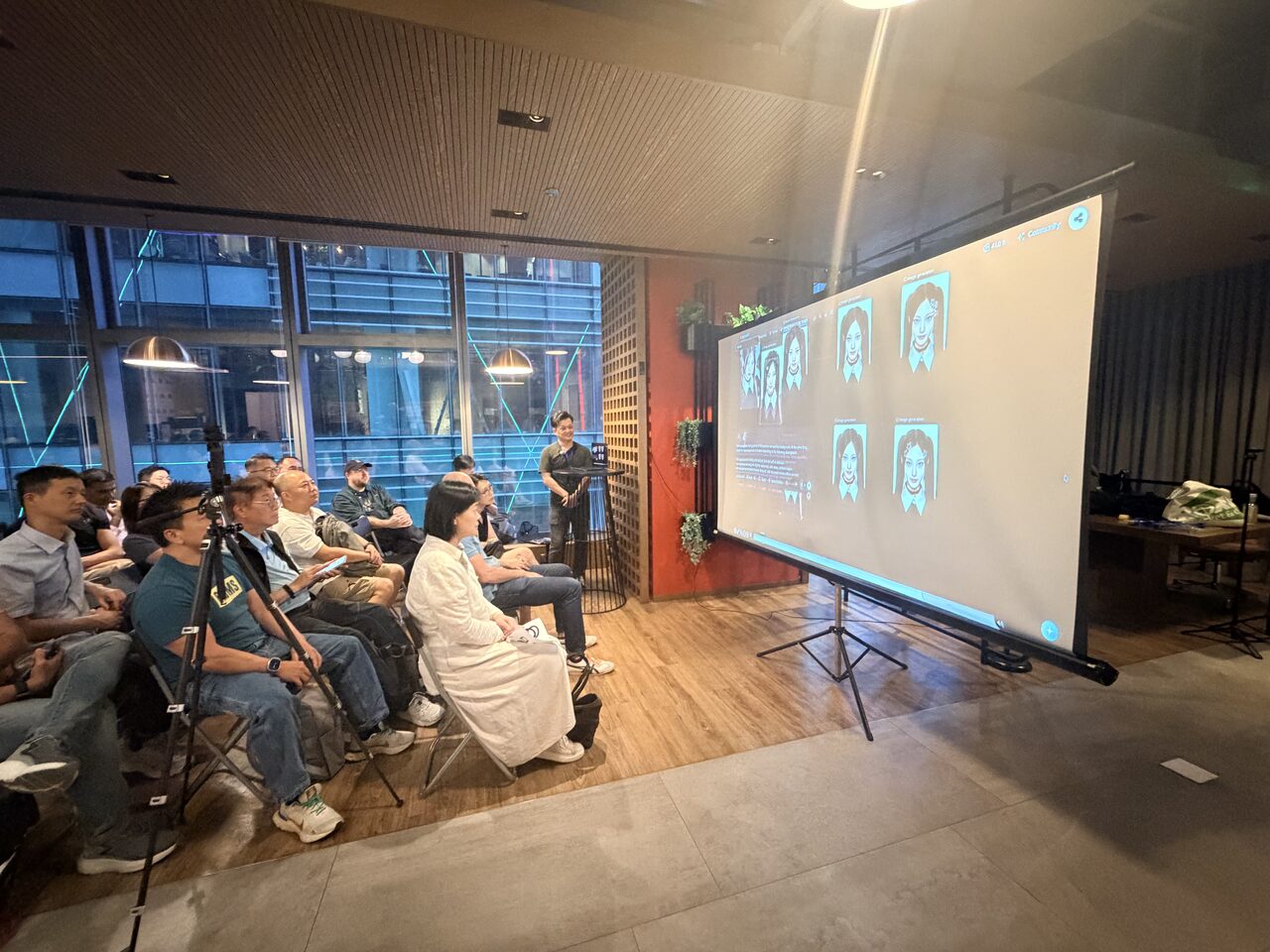 A packed audience watching a grid of AI-generated faces on the big screen