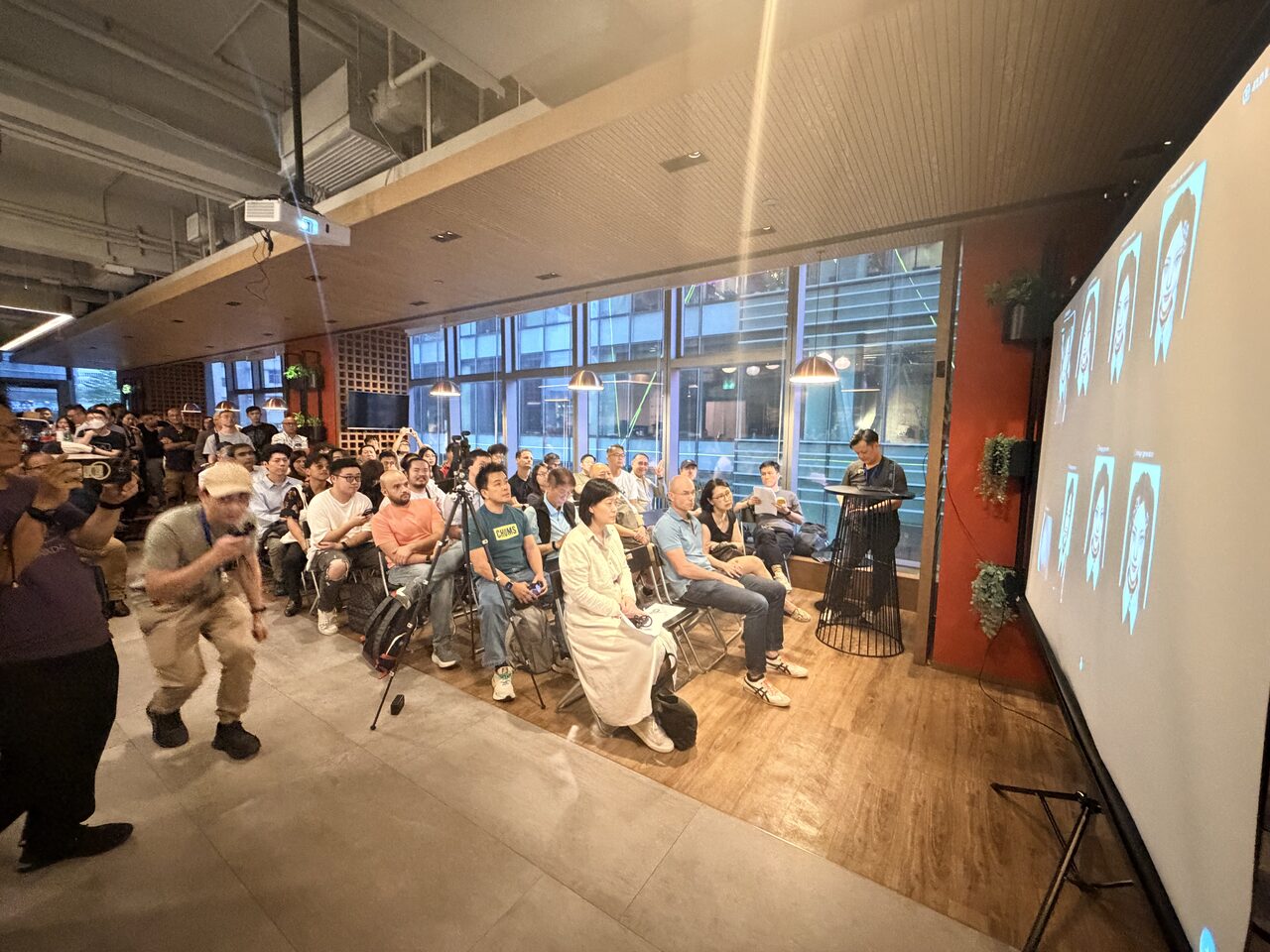 A wide view of the audience and a speaker at the screen